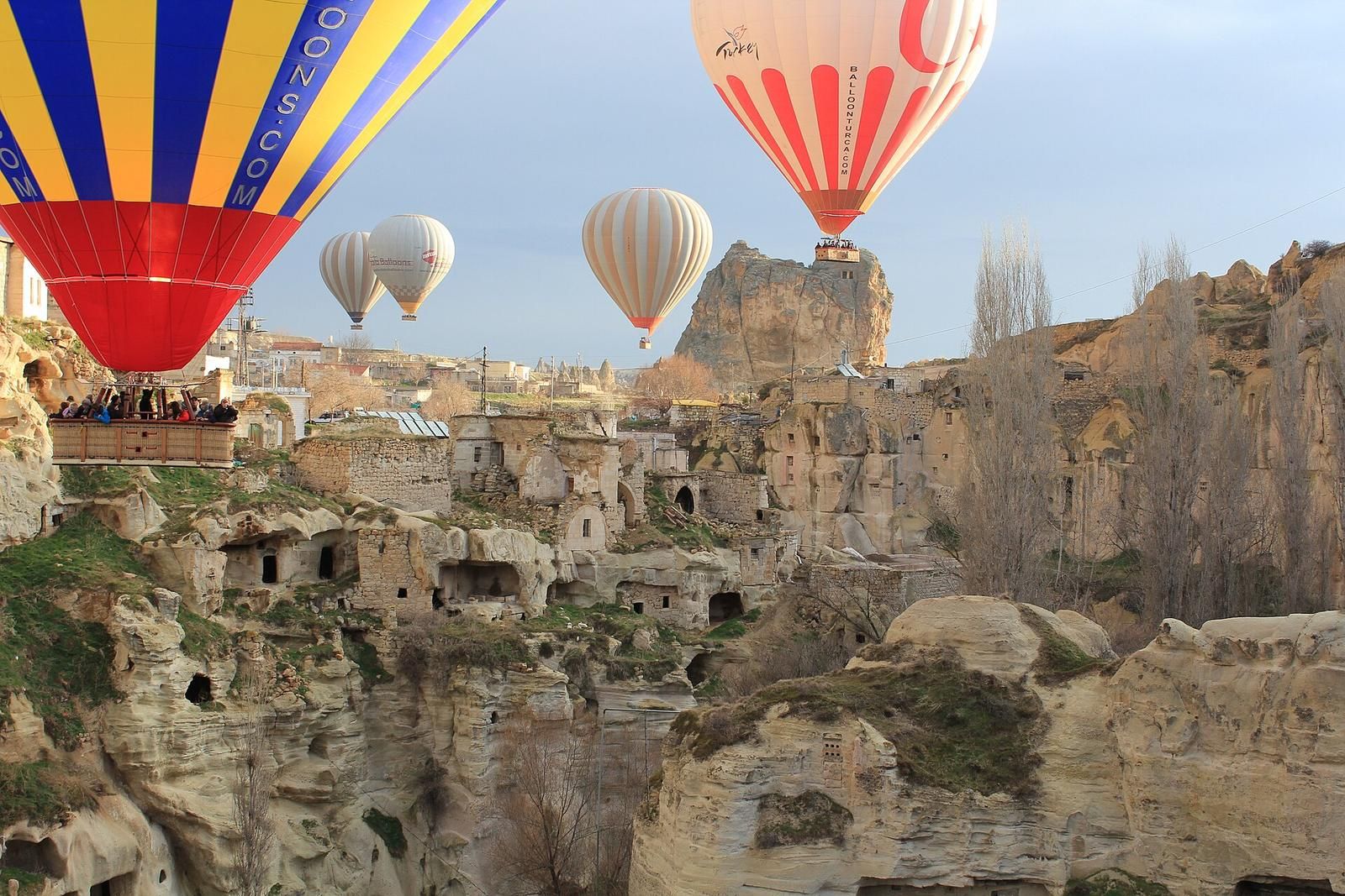 Balony przelatujące nisko nad skalnymi domami Ortahisar w Kapadocji