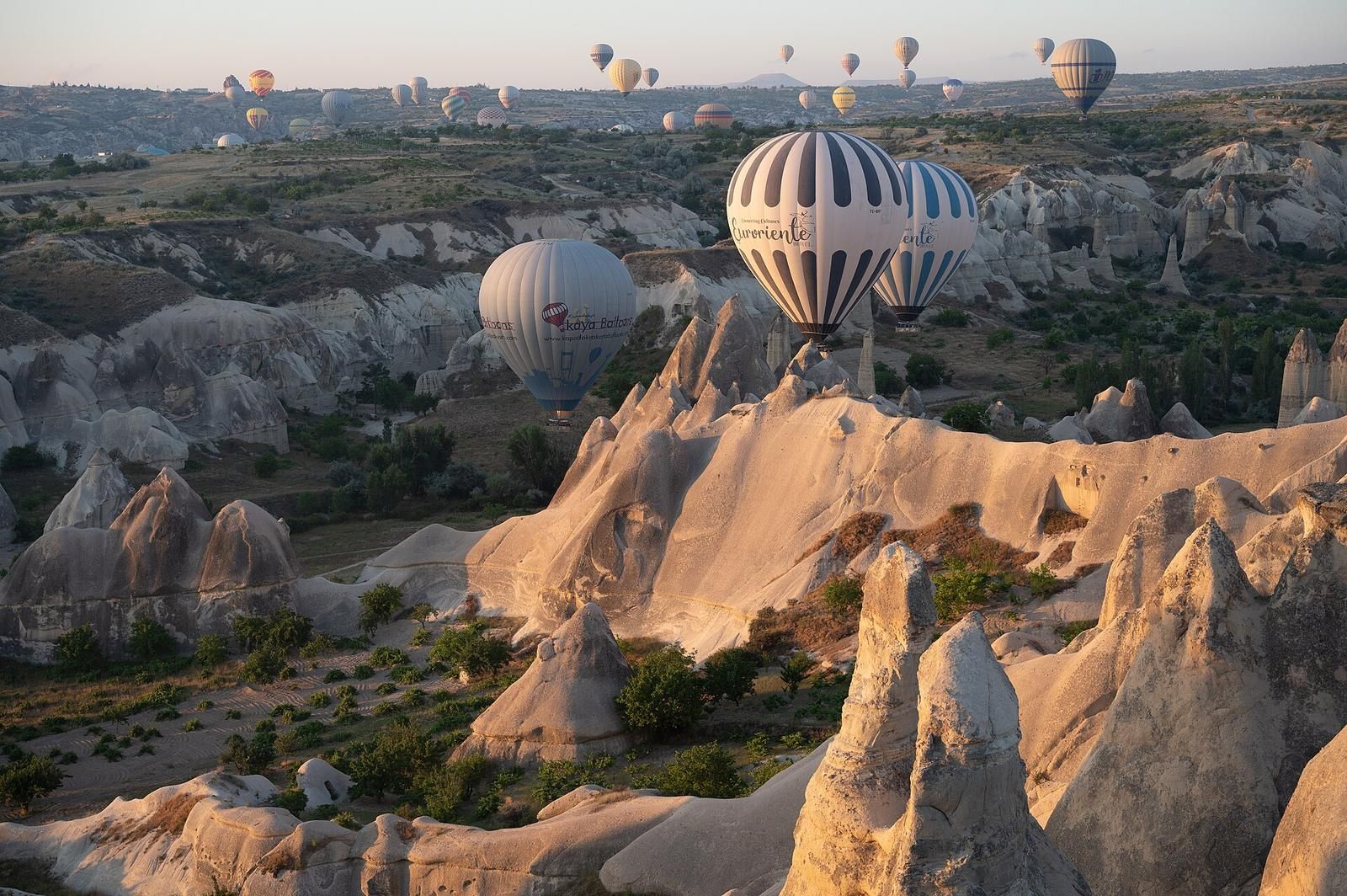 Balony lecące nisko nad formacjami skalnymi Parku Narodowego Göreme o poranku